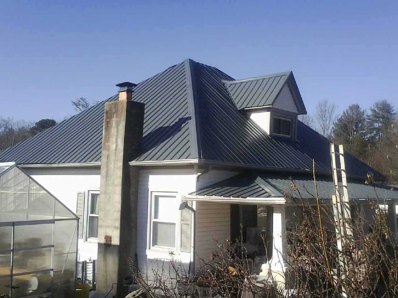 Dark blue standing seam metal roof on a white farmhouse with dormer — Slate & Tile Roof Repair by Roofing Brothers in Bigelow