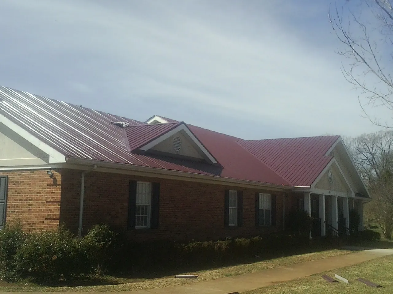 Red metal roof with gabled entries on a long brick building, from a Hail Damage Roof Repair job in Bigelow