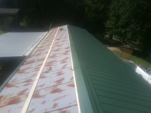 Old rusted panels beside newly installed green metal roofing — Wind Damage Roof Repair by Roofing Brothers in Bigelow