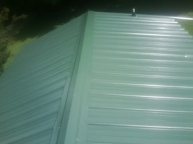 New green metal panels meeting at the ridge of a roof — Flat Roof Repair work by our crew in Bigelow