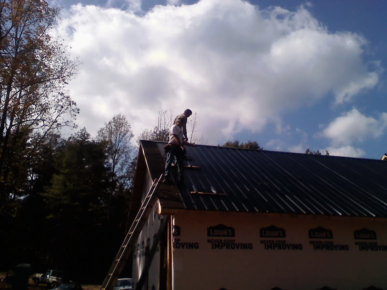 Roofer fastening dark metal panels high against a cloudy sky, from a Roof Inspection job in Bigelow