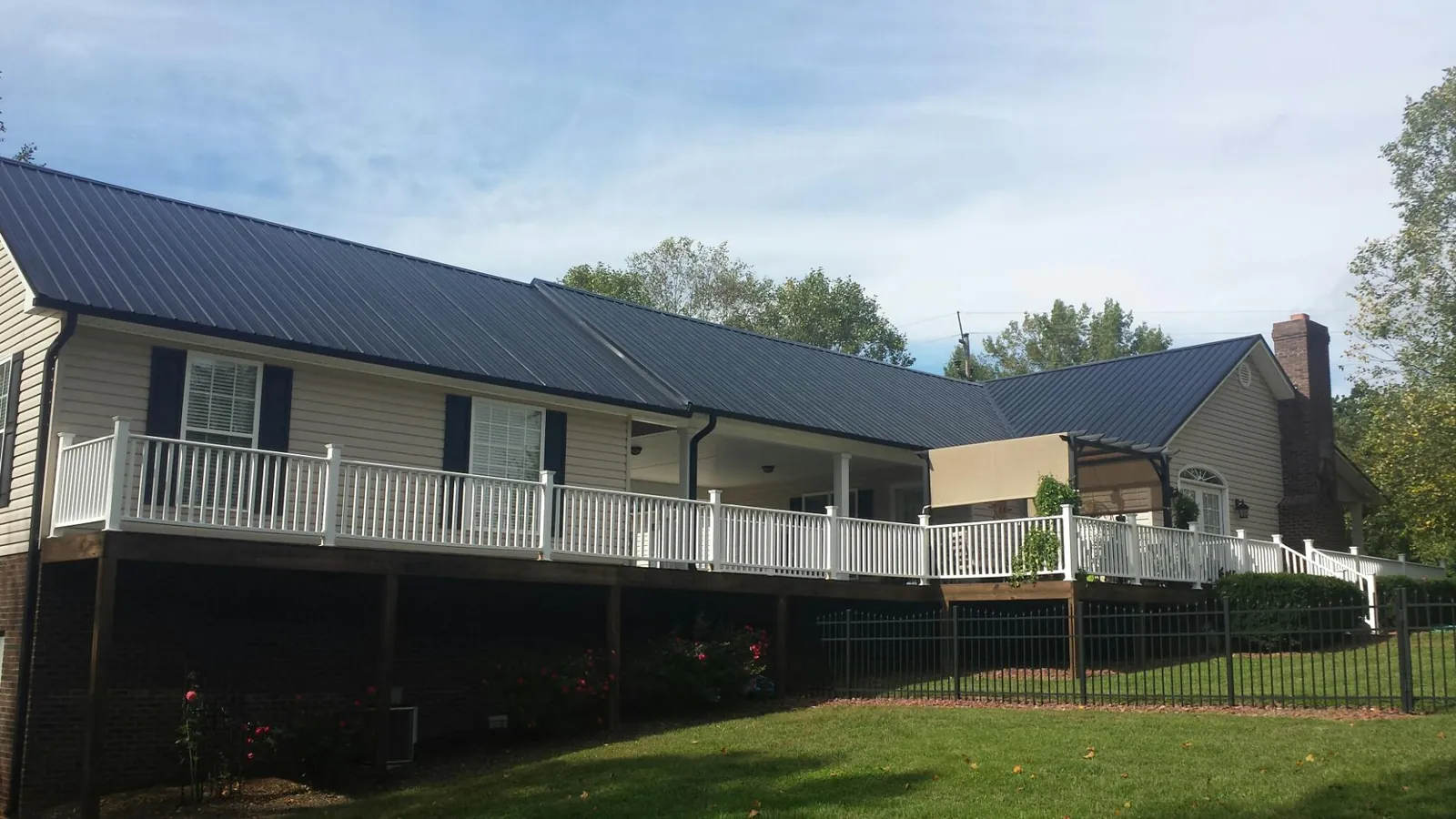 Black metal roof above a long white railed deck on a hillside home in Bigelow