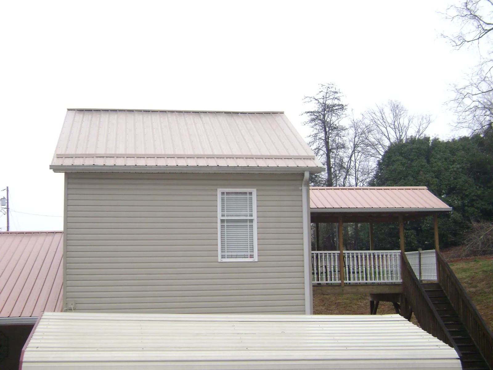 Tan metal roofs on a two story addition and attached porch, from a Roof Replacement job in Bigelow